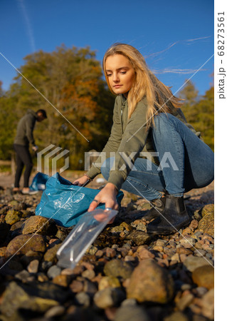 Serious young woman picking up plastic at rocky beach Serious young woman picking up plastic at rocky beach 68273561