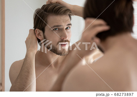 Close up anxious young man touching hair, looking in mirror 68273897