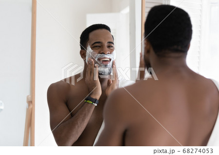 Mirror reflection smiling African American man applying shaving foam 68274053