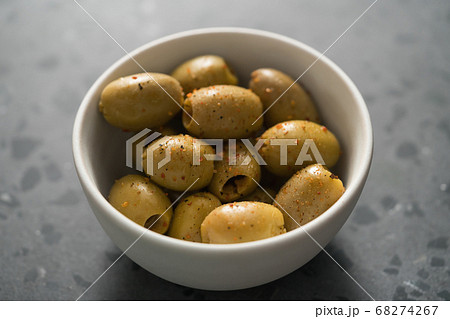 Closeup pitted whole green olives with spices in white bowl on terrazzo surface Closeup pitted whole green olives with spices in white bowl on terrazzo surface 68274267