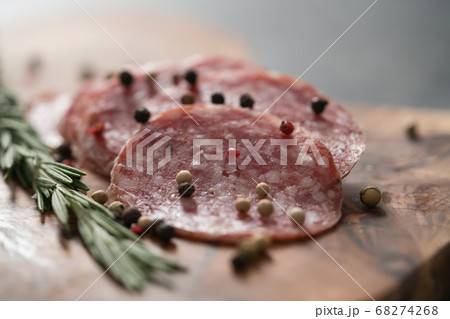 Sliced salame milano sausage on olive wood board with rosemary and pepper Sliced salame milano sausage on olive wood board with rosemary and pepper 68274268