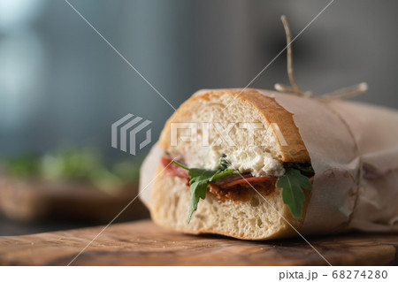 Ciabatta sandwich with salame, arugula, red pesto and cream cheese wrapped in paper on olive board Ciabatta sandwich with salame, arugula, red pesto and cream cheese wrapped in paper on olive board 68274280