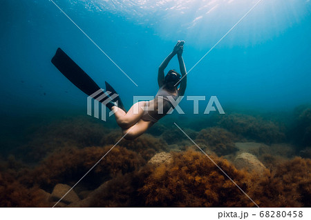 Sporty woman freediver with fins glides underwater in blue sea. Freediving in ocean 68280458