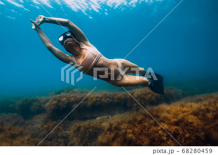 Sporty woman freediver with fins glides underwater in blue sea. Freediving in ocean Sporty woman freediver with fins glides underwater in blue sea. Freediving in ocean 68280459
