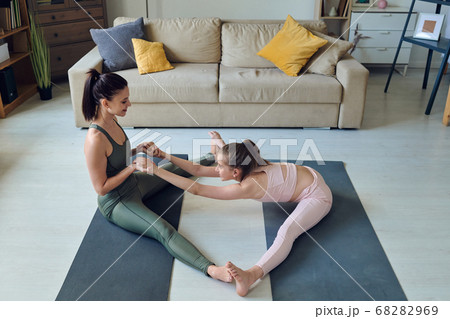 Pretty young woman helping her positive teenage daughter with yoga exercise 68282969