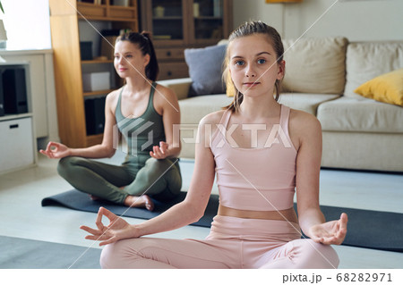 Pretty active teenager in pink tracksuit meditating with mother in living-room Pretty active teenager in pink tracksuit meditating with mother in living-room 68282971