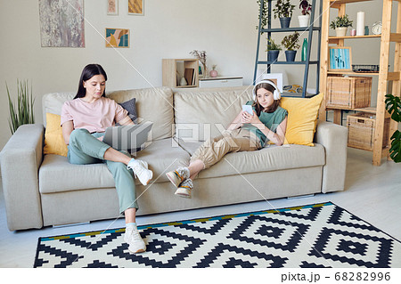 Pretty teenager in headphones and her serious mother in casualwear using gadgets 68282996