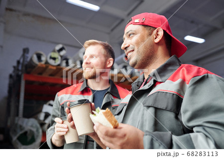 Two happy young intercultural male workers with sandwiches and coffee 68283113