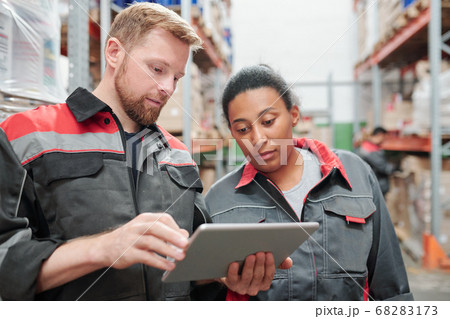 Young bearded engineer or worker of warehouse and his colleague using tablet Young bearded engineer or worker of warehouse and his colleague using tablet 68283173