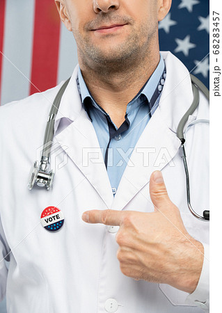 Hand of contemporary mature American clinician in whitecoat pointing at insignia Hand of contemporary mature American clinician in whitecoat pointing at insignia 68283457