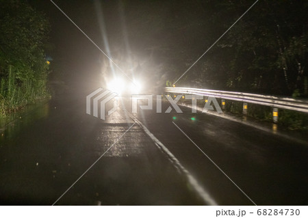 雨の夜の山道ですれ違うライトをつけた対向車の写真素材