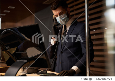 Professional receptionist in medical mask receiving phone calls Professional receptionist in medical mask receiving phone calls 68286754
