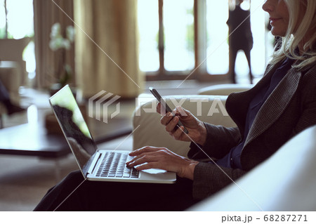 Determined lady holding her smartphone while being seated in a waiting area Determined lady holding her smartphone while being seated in a waiting area 68287271