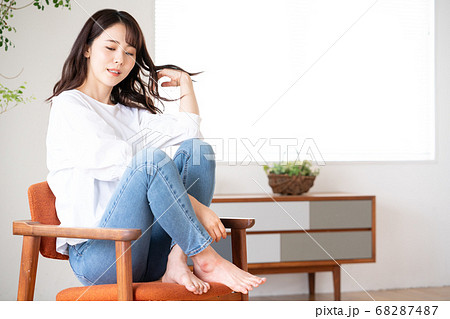 リビングで椅子の上にあぐらをかいて座る若い女性の写真素材