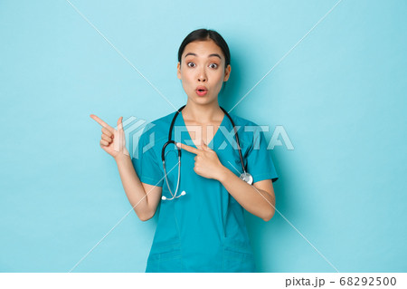 Covid-19, social distancing and coronavirus pandemic concept. Professional doctor, female nurse or physician in scrubs inform patients, pointing fingers upper left corner, showing clinic banner. Covid-19, social distancing and coronavirus pandemic concept. Professional doctor, female nurse or physician in scrubs inform patients, pointing fingers upper left corner, showing clinic banner. 68292500