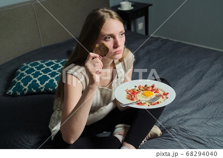 Girl sitting on bed with remote control watching TV and eating 68294040