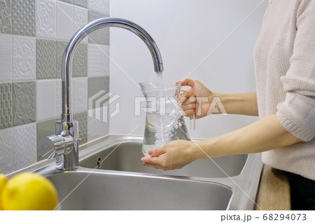 Woman pouring water into jug from kitchen faucet Woman pouring water into jug from kitchen faucet 68294073