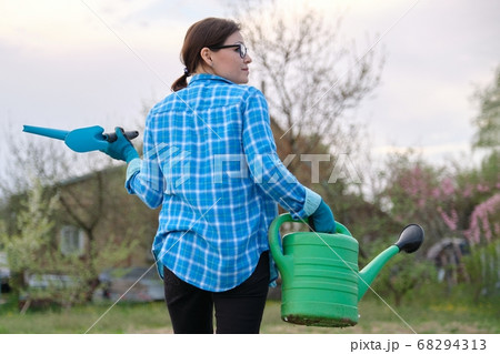 Female gardener holding watering can and garden tools Female gardener holding watering can and garden tools 68294313