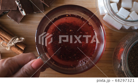 Process of brewing red karkade tea, close up top view. Concept. Cup of freshly brewed fruit tea, pouring hot water from the kettle into a glass cup on wooden background. Process of brewing red karkade tea, close up top view. Concept. Cup of freshly brewed fruit tea, pouring hot water from the kettle into a glass cup on wooden background. 68297321