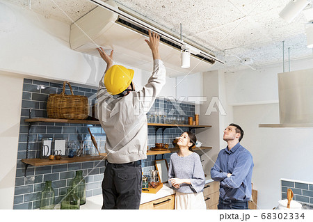 黄色いヘルメットをかぶって、エアコンを点検する修理業者 68302334