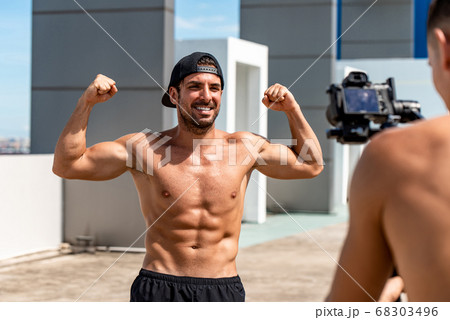 Happy muscular Hispanic man fitness vlogger flexing his arm muscles while recording  68303496