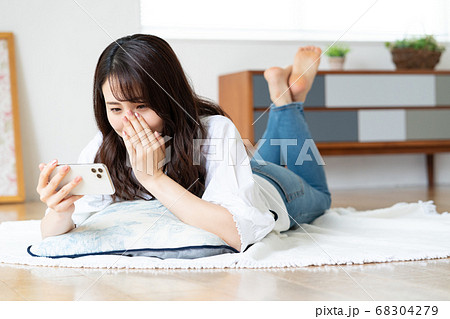 リビングで寝転がりながら動画を見て泣く若い女性 68304279