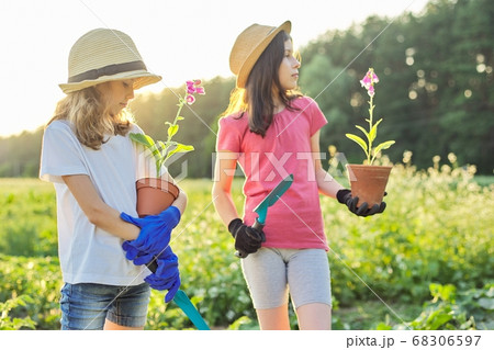 Portrait of two little gardeners in gloves with flowering plants in pots and garden shovels 68306597
