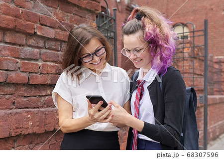 Female student walking and talking with woman teacher, girl showing on smartphone screen 68307596