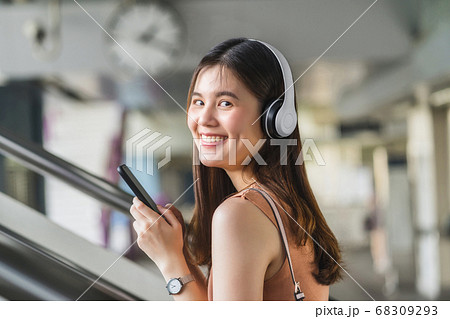 Young Asian woman passenger wearing headphone and using smart mobile phone to listening music and walking up the stairs in subway station when traveling in big city, commuter and transportation concept 68309293