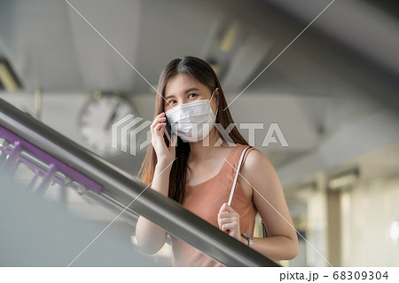 Young Asian woman passenger wearing surgical mask and using mobile phone for talking when walking up the stairs in subway station while traveling at Covid19 outbreak, Infection and Pandemic concept Young Asian woman passenger wearing surgical mask and using mobile phone for talking when walking up the stairs in subway station while traveling at Covid19 outbreak, Infection and Pandemic concept 68309304