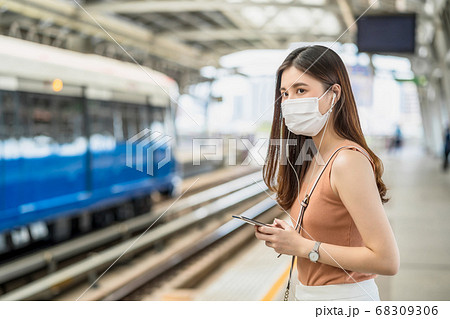 Young Asian woman passenger wearing surgical mask and listening music via smart mobile phone in subway train when traveling in big city at Covid19 outbreak, Infection and Pandemic concept Young Asian woman passenger wearing surgical mask and listening music via smart mobile phone in subway train when traveling in big city at Covid19 outbreak, Infection and Pandemic concept 68309306