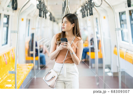 Young Asian woman passenger using smart mobile phone and looking to outside of subway train when traveling in big city, commuter and transportation concept 68309307