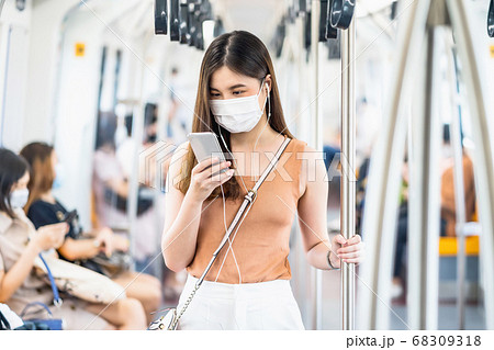 Young Asian woman passenger wearing surgical mask and listening music via smart mobile phone in subway train when traveling in big city at Covid19 outbreak, Infection and Pandemic concept Young Asian woman passenger wearing surgical mask and listening music via smart mobile phone in subway train when traveling in big city at Covid19 outbreak, Infection and Pandemic concept 68309318
