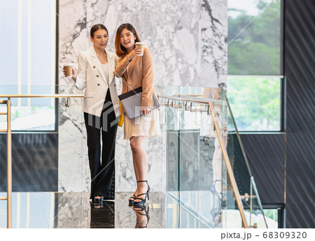 Two asian businesswomen walking and talking during coffee break in modern office or coworking space, coffee break, relaxing and talking after working time, business and people partnership concept Two asian businesswomen walking and talking during coffee break in modern office or coworking space, coffee break, relaxing and talking after working time, business and people partnership concept 68309320