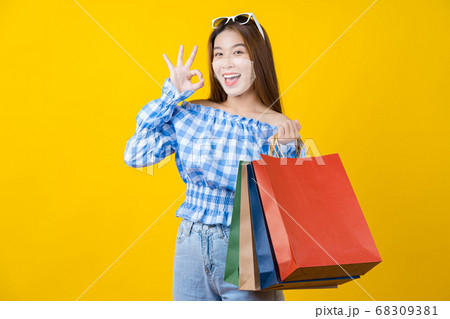 Attractive Asian smiling young woman wearing technology augmented reality surgical mask in covid19 outbreak and Carrying a shopping coloful bag and gesturing ok sign to agreement on yellow background Attractive Asian smiling young woman wearing technology augmented reality surgical mask in covid19 outbreak and Carrying a shopping coloful bag and gesturing ok sign to agreement on yellow background 68309381