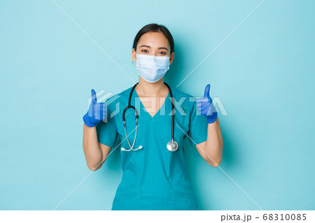 Covid-19, social distancing and coronavirus pandemic concept. Optimistic smiling asian female doctor, physician in medical mask, rubber gloves and scrubs, showing thumbs-up, guarantee quality checkup 68310085