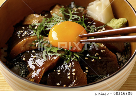 ガリやワサビや刻んだ海苔が乗った鰹の漬け丼の卵黄を割るの写真素材