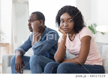 Frustrated african man and woman sitting on couch at home Frustrated african man and woman sitting on couch at home 68317229