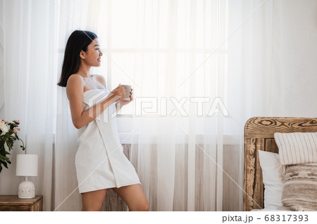 Asian girl drinking coffee and looking through window 68317393