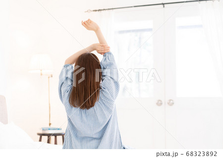 朝起きてベッドで伸びをする若い女性の後ろ姿 68323892