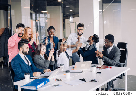 Young multi-ethnic work team exchanges ideas gathering around laptop computers 68330687