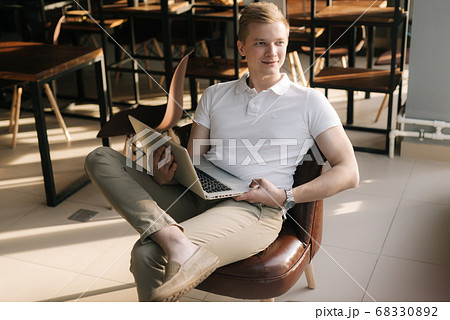 Smiling young businessman wearing fashion casual clothing sitting on chair and holding laptop. 68330892