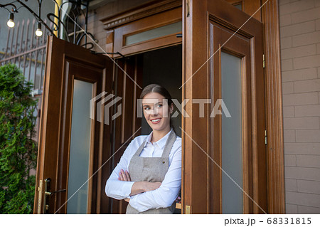 Charming young waitress leaning on door, crossing her arms Charming young waitress leaning on door, crossing her arms 68331815