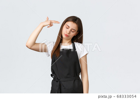 Grocery store employees, small business and coffee shops concept. Annoyed and tired saleswoman in black apron pointing fake gun at head irritated, staring skeptical and bothered 68333054