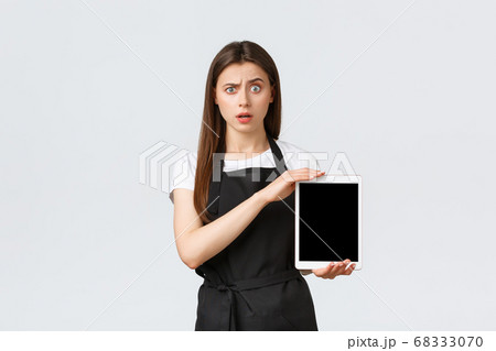 Grocery store employees, small business and coffee shops concept. Confused and puzzled cute girl barista in black apron raise eyebrow shocked and showing digital tablet screen Grocery store employees, small business and coffee shops concept. Confused and puzzled cute girl barista in black apron raise eyebrow shocked and showing digital tablet screen 68333070