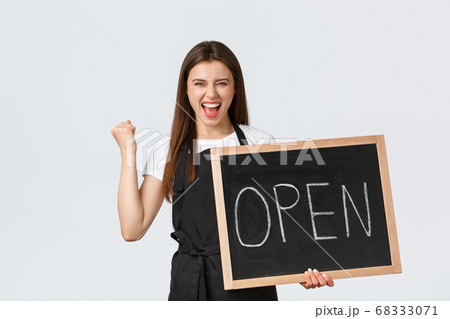 Grocery store employees, small business and coffee shops concept. Rejoicing happy barista in black apron fist pump triumphing that cafe finally open, showing sign, standing white background Grocery store employees, small business and coffee shops concept. Rejoicing happy barista in black apron fist pump triumphing that cafe finally open, showing sign, standing white background 68333071