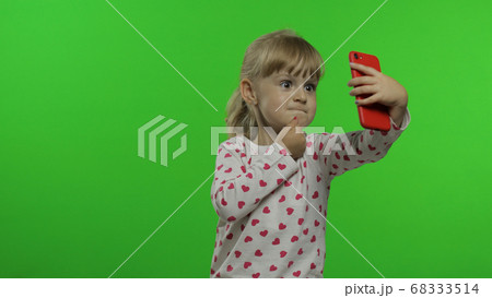 Kid girl using smartphone. Child emotionally makes selfie on mobile phone. Video call, blog, game Kid girl using smartphone. Child emotionally makes selfie on mobile phone. Video call, blog, game 68333514