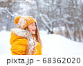 Outdoor close-up portrait of young beautiful happy smiling girl, wearing yellow jacket and knitted hat walking in winter park 68362020