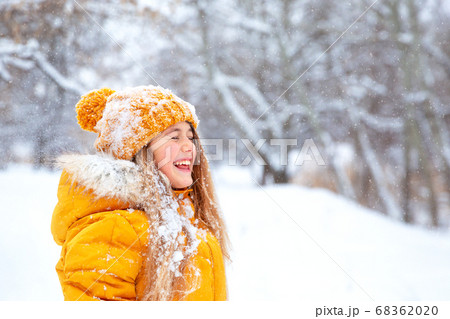 Outdoor close-up portrait of young beautiful happy smiling girl, wearing yellow jacket and knitted hat walking in winter park 68362020