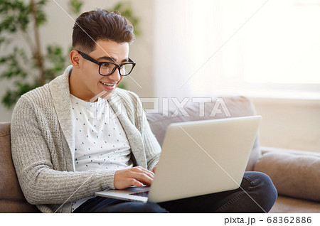 Cheerful ethnic guy using laptop on sofa 68362886
